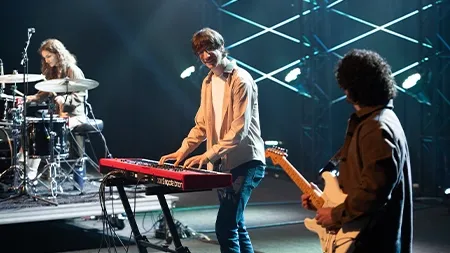 Students playing keyboard, guitar, and drums onstage in chapel