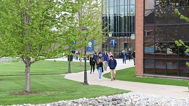 Students walking on campus by a glass and brick building in the summer.